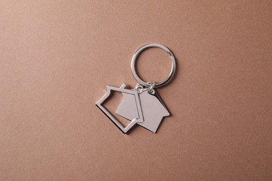 Photo of Metallic keychains in shape of houses on light brown background, top view