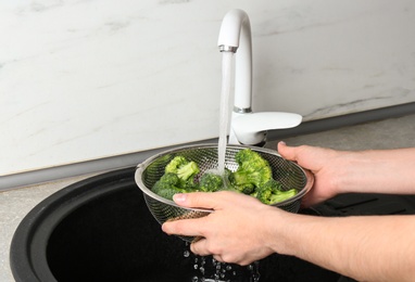 Photo of Woman washing fresh green broccoli in metal colander under tap water, closeup view. Space for text