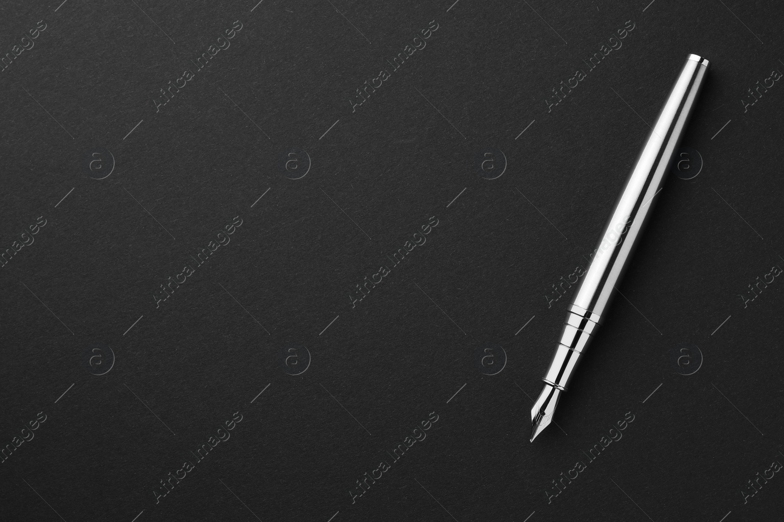 Photo of Stylish silver fountain pen on black background, top view. Space for text