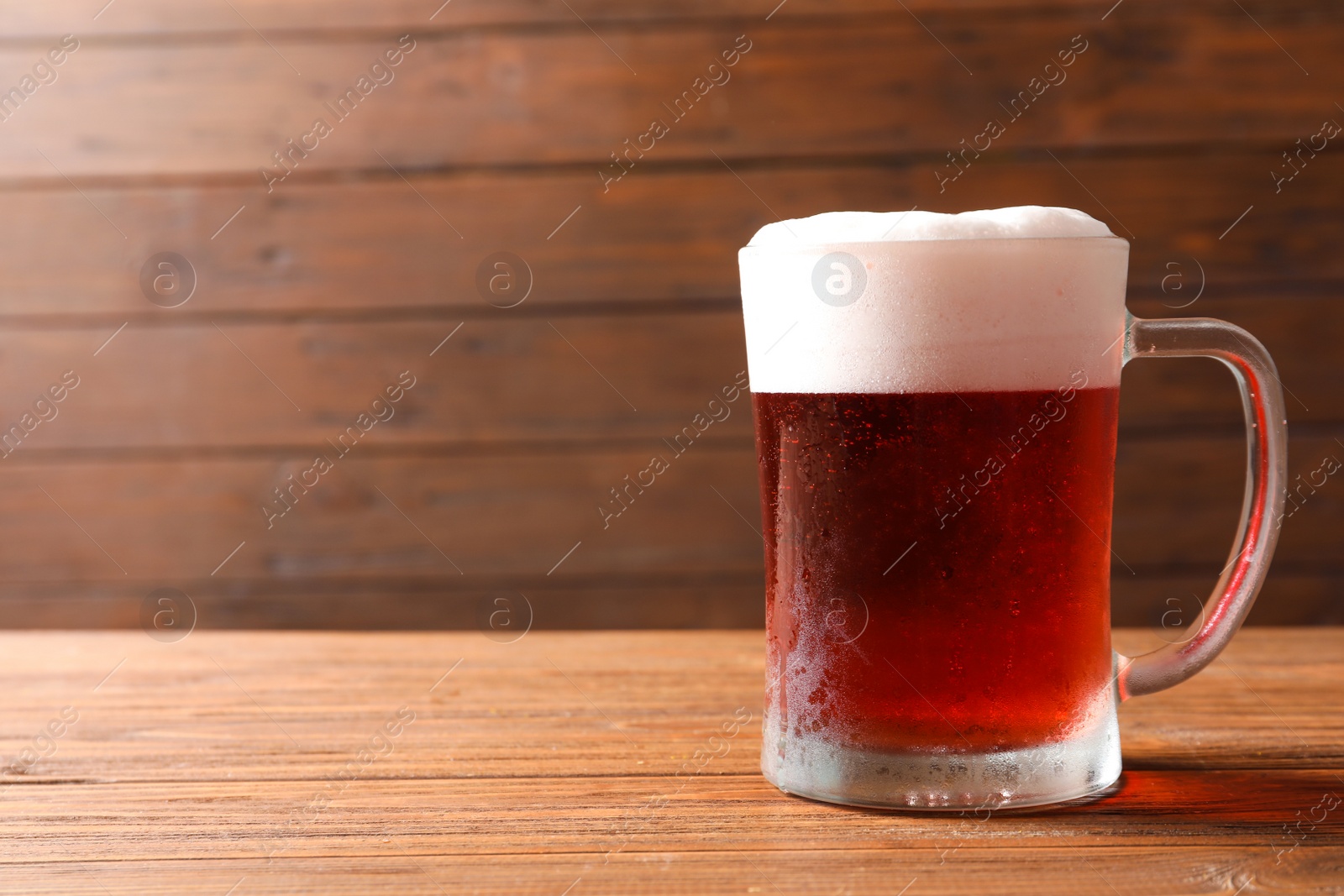 Photo of Glass mug with cold red beer on wooden table