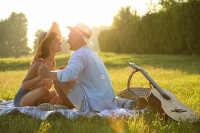 Photo of Happy couple with guitar and picnic basket in park on sunny day