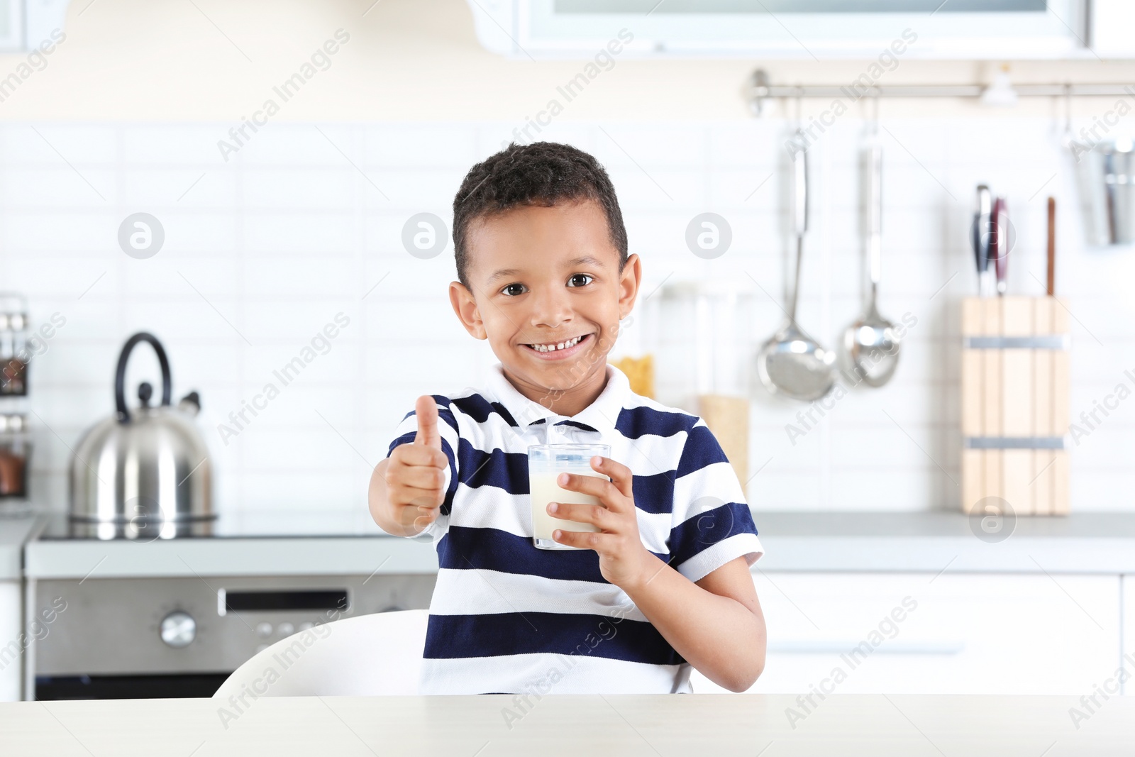 Photo of Adorable African-American boy with glass of milk in kitchen