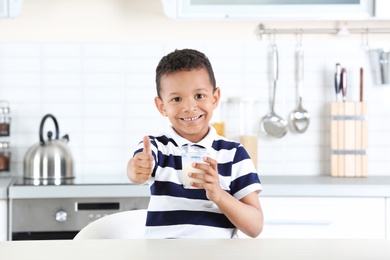 Photo of Adorable African-American boy with glass of milk in kitchen