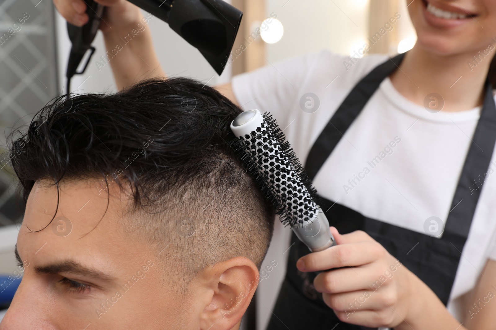 Photo of Professional hairdresser drying client's hair in salon, closeup