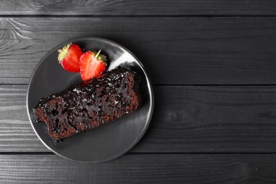 Photo of Piece of tasty chocolate sponge cake with strawberries on black wooden table, top view. Space for text