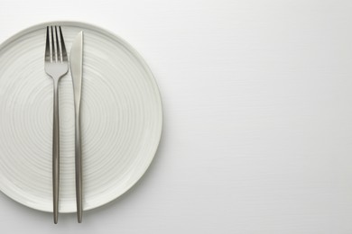 Photo of Clean plate, fork and knife on white table, top view. Space for text