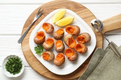 Photo of Delicious cooked snails served on white wooden table, flat lay