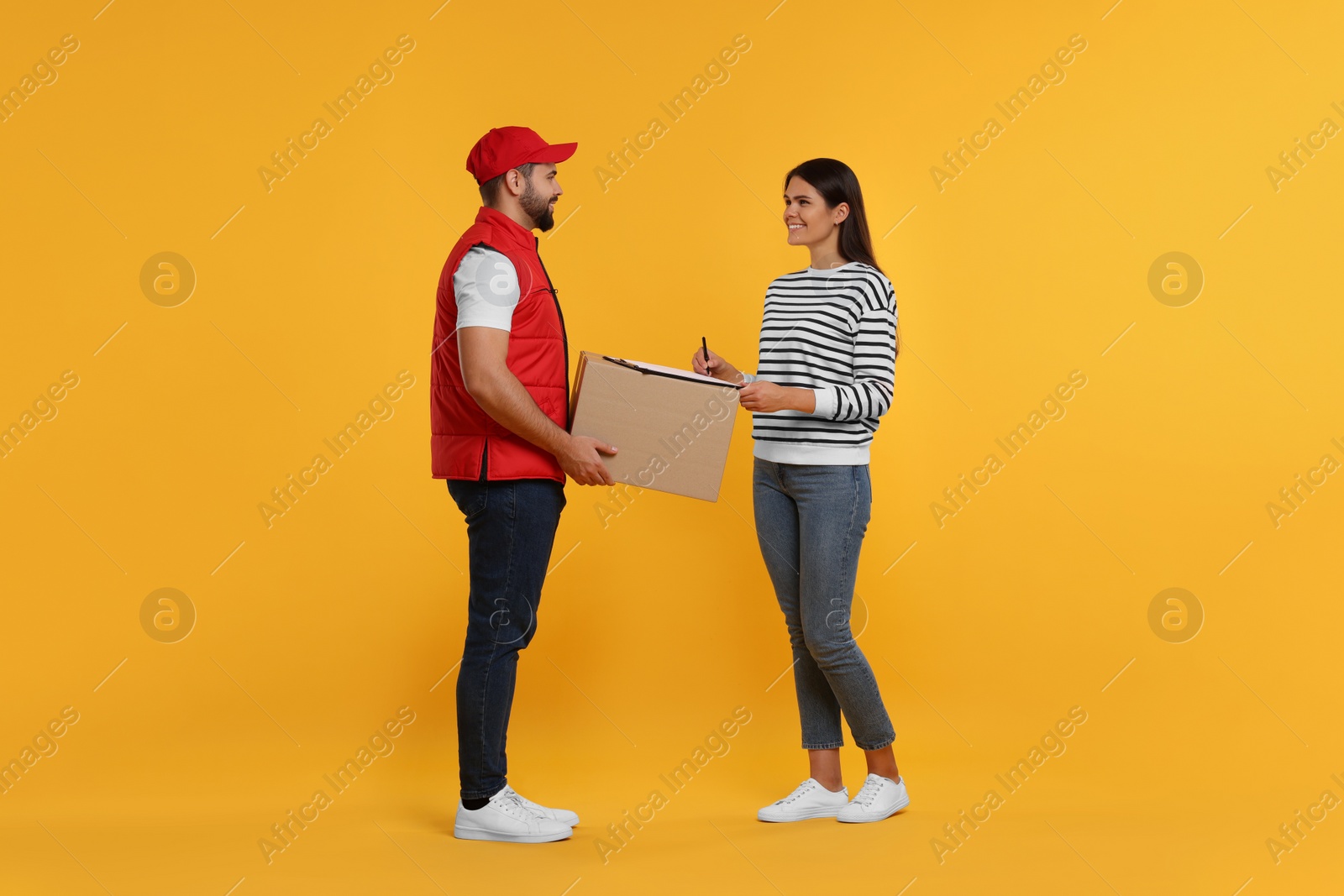 Photo of Happy young woman signing order receipt on orange background. Courier delivery