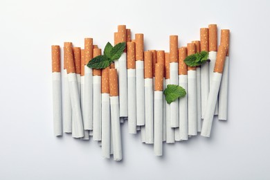 Photo of Menthol cigarettes and fresh mint leaves on white background, flat lay