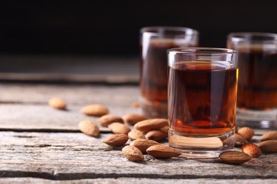 Photo of Shot glasses with tasty amaretto liqueur and almonds on wooden table, closeup. Space for text