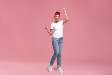Happy young woman in stylish headband dancing on pink background