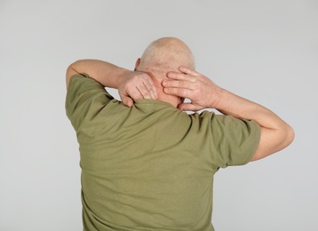 Photo of Senior man suffering from pain in neck on light background