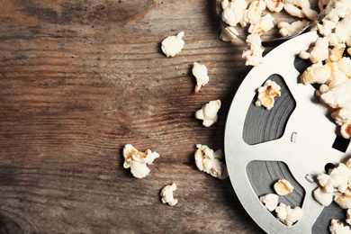 Photo of Tasty popcorn and film reel on wooden background, top view with space for text