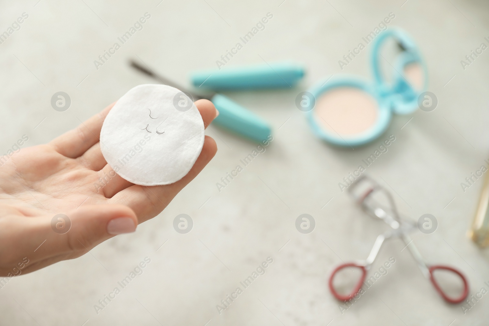 Photo of Young woman holding cotton pad with fallen eyelashes over table