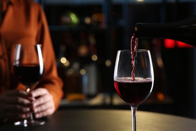 Pouring red wine from bottle into glass on table indoors, closeup. Space for text