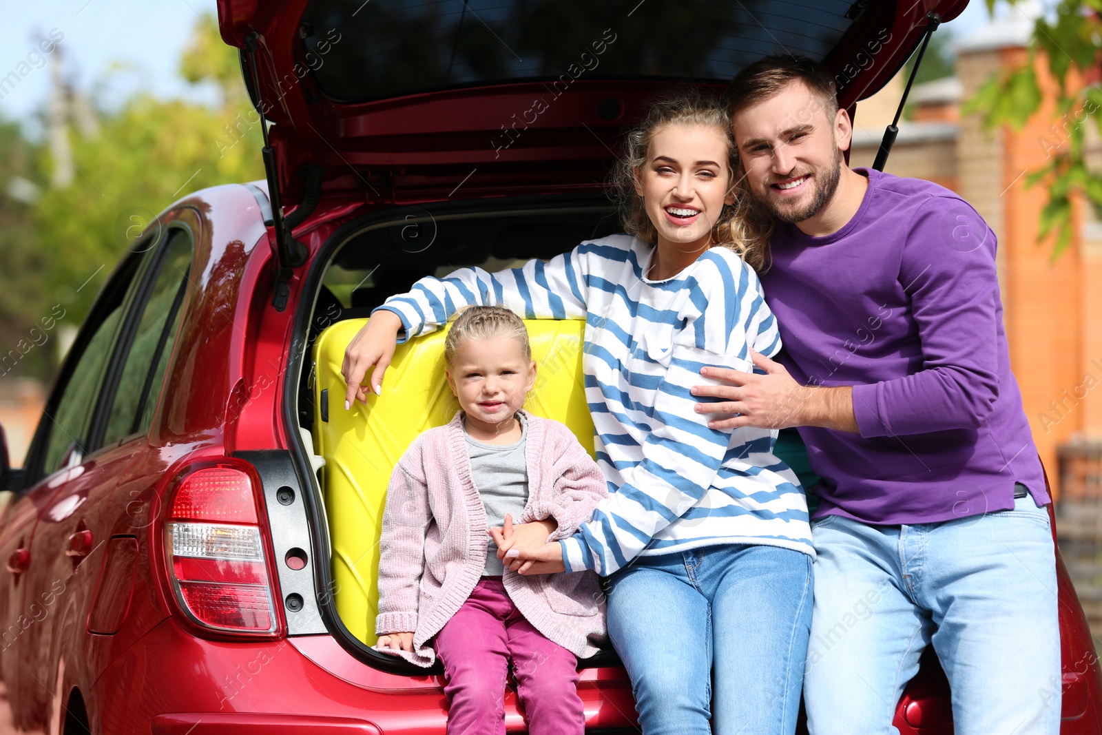 Photo of Young family having rest near car trunk loaded with suitcase outdoors