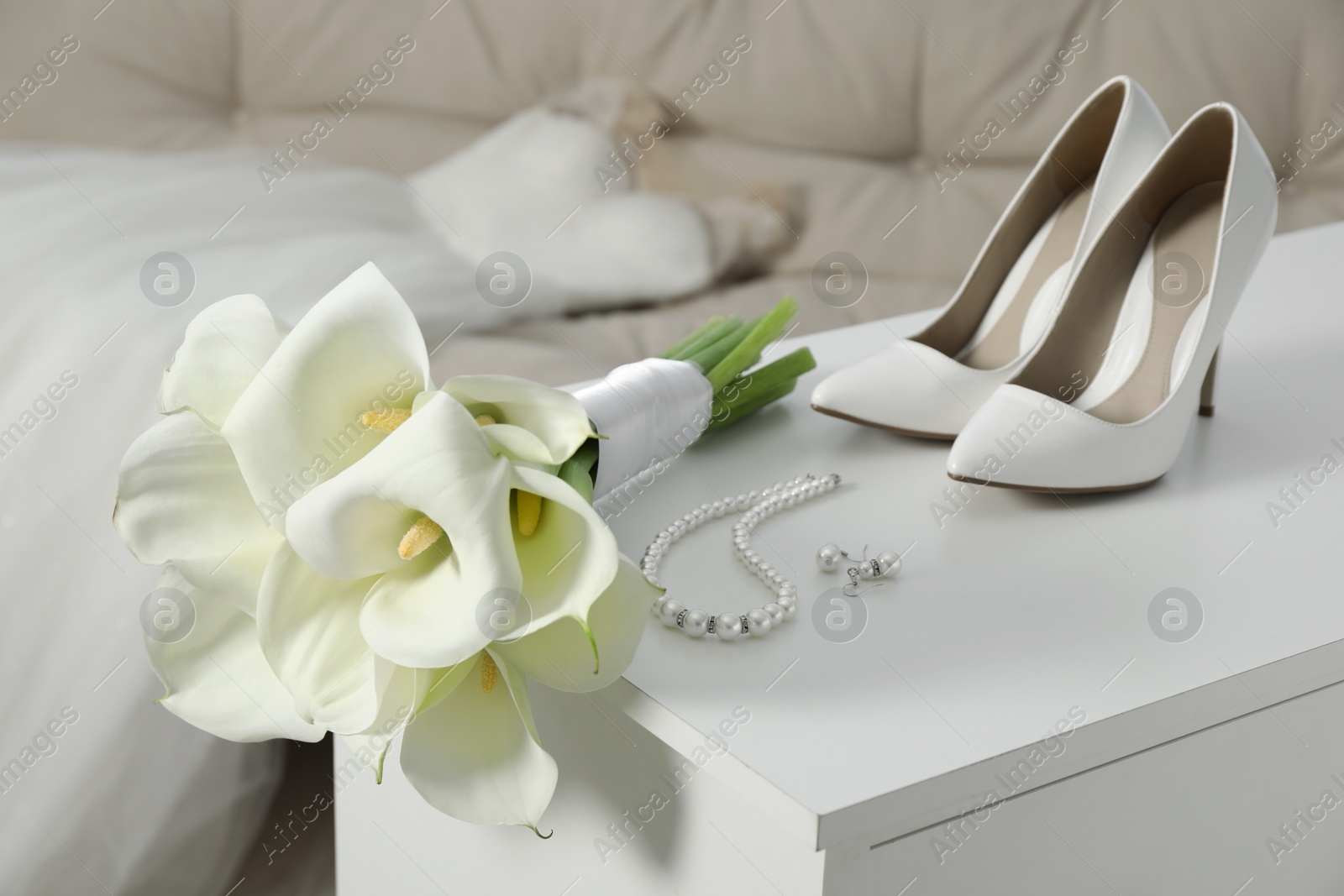 Photo of Beautiful calla lily flowers tied with ribbon, shoes and jewelry on white chest of drawers indoors