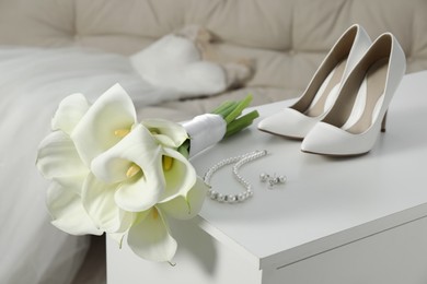 Beautiful calla lily flowers tied with ribbon, shoes and jewelry on white chest of drawers indoors