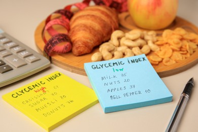 Photo of Glycemic index. Notes with information, measuring tape, calculator, pen and products on beige background, closeup
