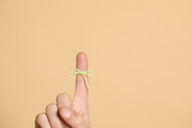 Photo of Man showing index finger with tied bow as reminder on beige background, closeup. Space for text