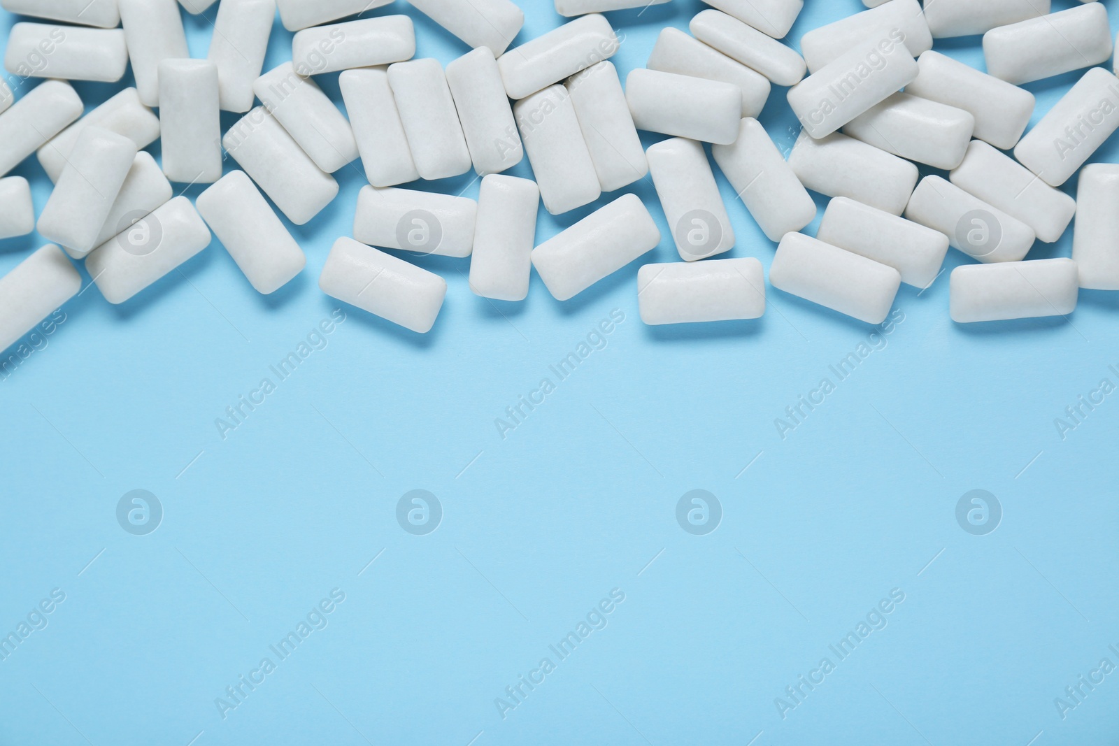 Photo of Tasty white chewing gums on light blue background, flat lay. Space for text