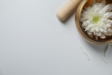 Photo of Tibetan singing bowl with water, beautiful chrysanthemum flower and mallet on white background, top view. Space for text