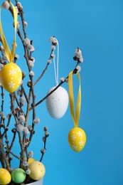 Photo of Beautiful willow branches with painted eggs on light blue background, space for text. Easter decor
