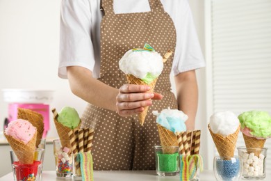 Photo of Woman holding waffle cone with cotton candy indoors, closeup