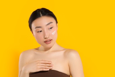 Photo of Beautiful young woman with sun protection cream on her face against orange background, space for text