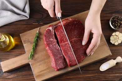 Photo of Woman cutting fresh raw beef steak at wooden table, top view