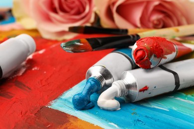 Photo of Tubes of colorful oil paints and brush on canvas with abstract painting, closeup
