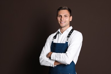 Portrait of happy young waiter in uniform on brown background