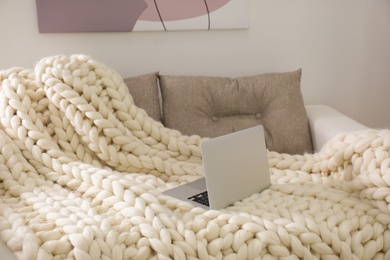 Soft knitted blanket and modern laptop on couch in living room. Interior element