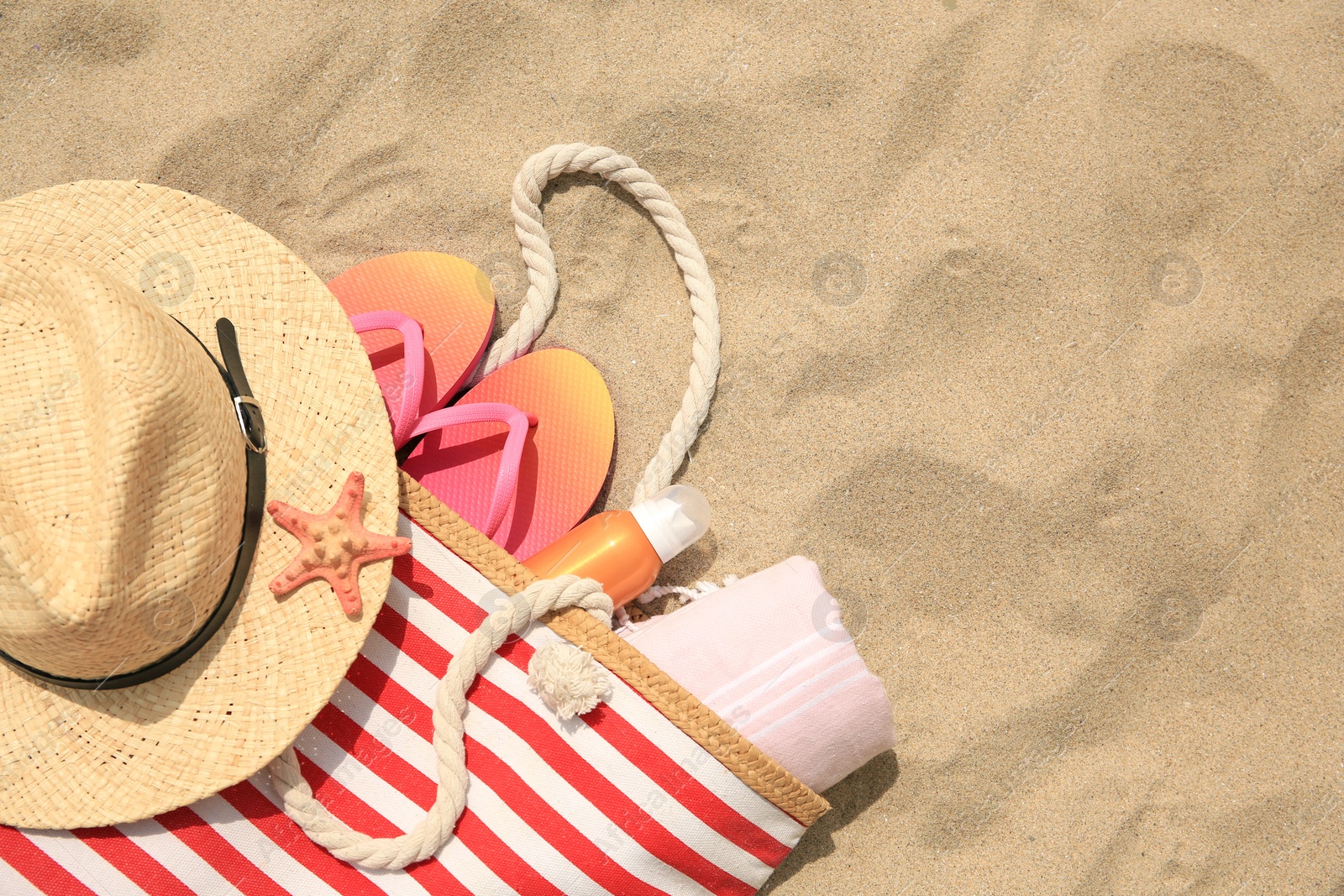 Photo of Stylish striped bag with beach accessories on sand, flat lay. Space for text