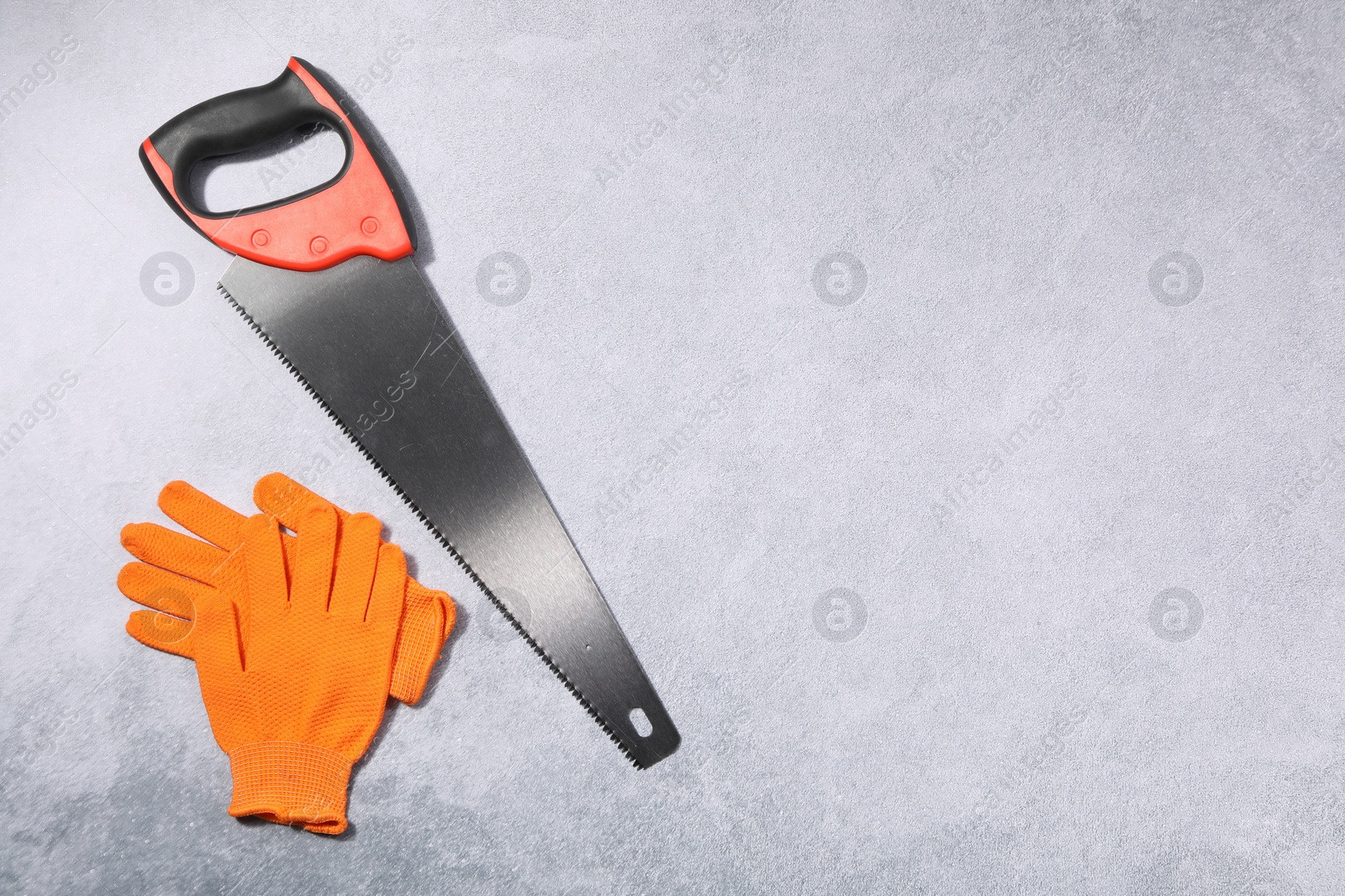 Photo of Saw with colorful handle and gloves on gray background, flat lay. Space for text