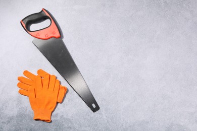 Saw with colorful handle and gloves on gray background, flat lay. Space for text