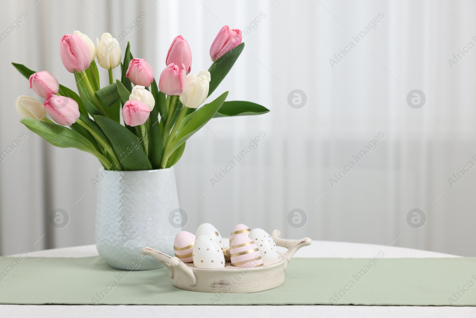 Photo of Easter decorations. Bouquet of tulips and painted eggs on white table indoors. Space for text