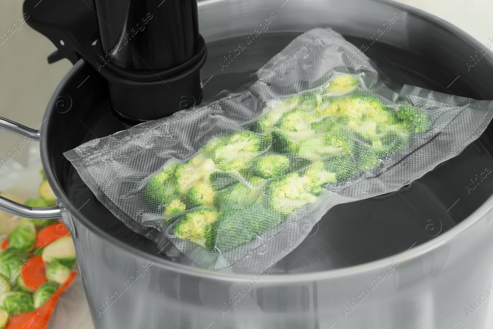 Photo of Sous vide cooker and vacuum packed broccoli in pot on table, closeup. Thermal immersion circulator