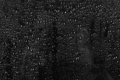 Photo of Glass with rain drops against dark background