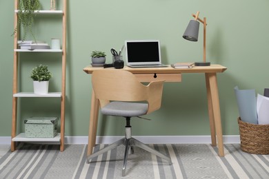 Workplace with laptop, stationery on desk and chair in home office