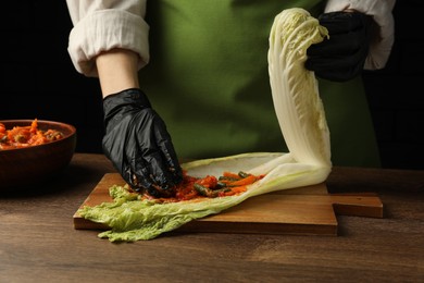 Woman preparing spicy cabbage kimchi at wooden table against dark background, closeup