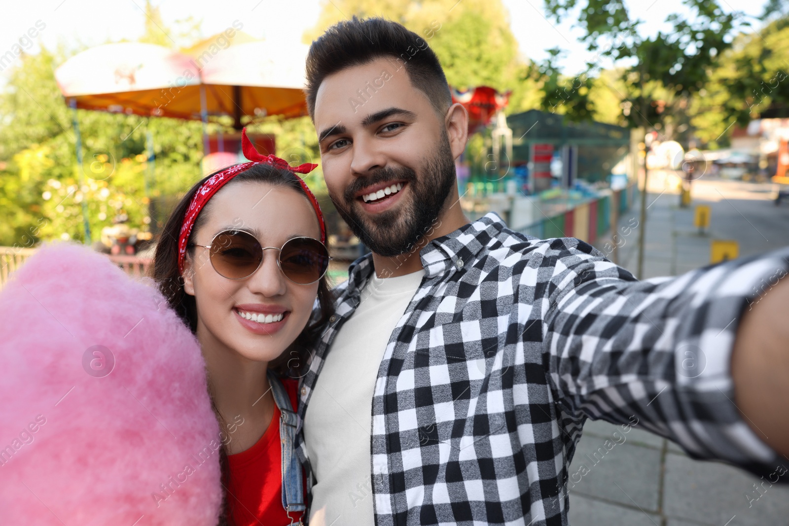 Photo of Happy young man and his girlfriend with cotton candy taking selfie at funfair