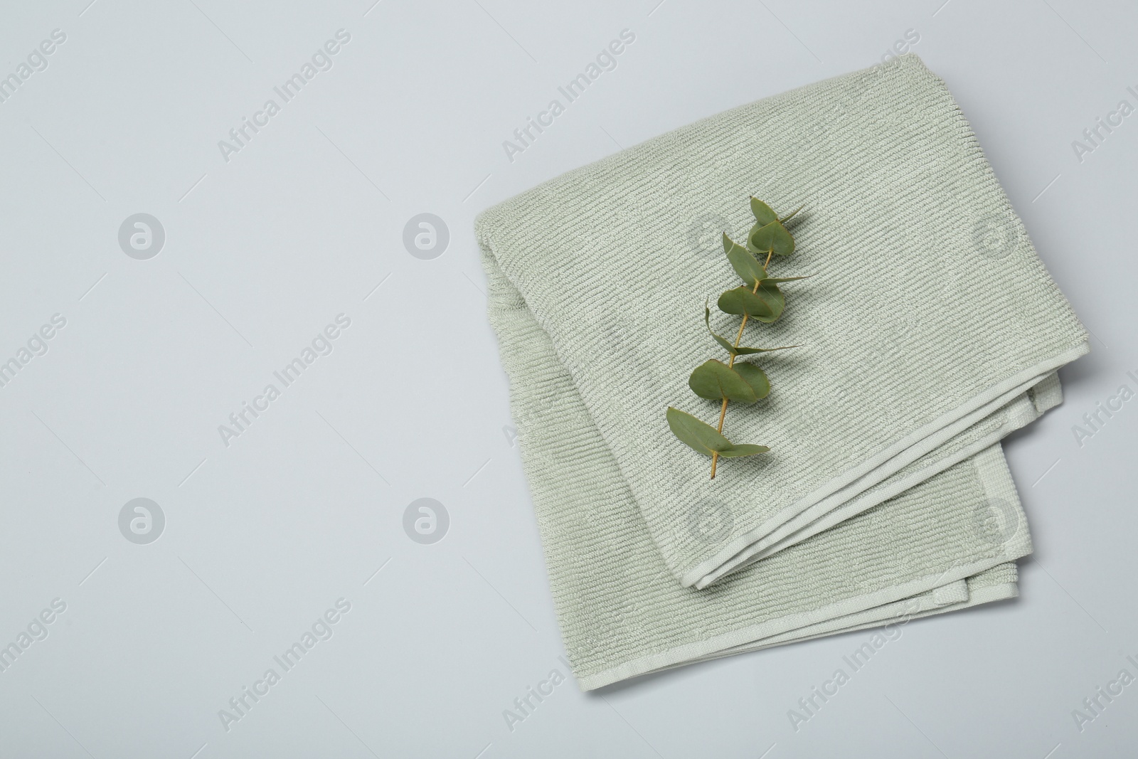 Photo of Soft green towel and eucalyptus branch on light grey background, top view. Space for text