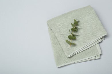 Photo of Soft green towel and eucalyptus branch on light grey background, top view. Space for text