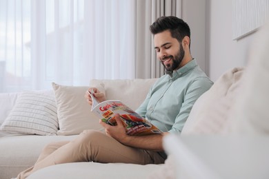 Photo of Young man reading culinary magazine on sofa at home