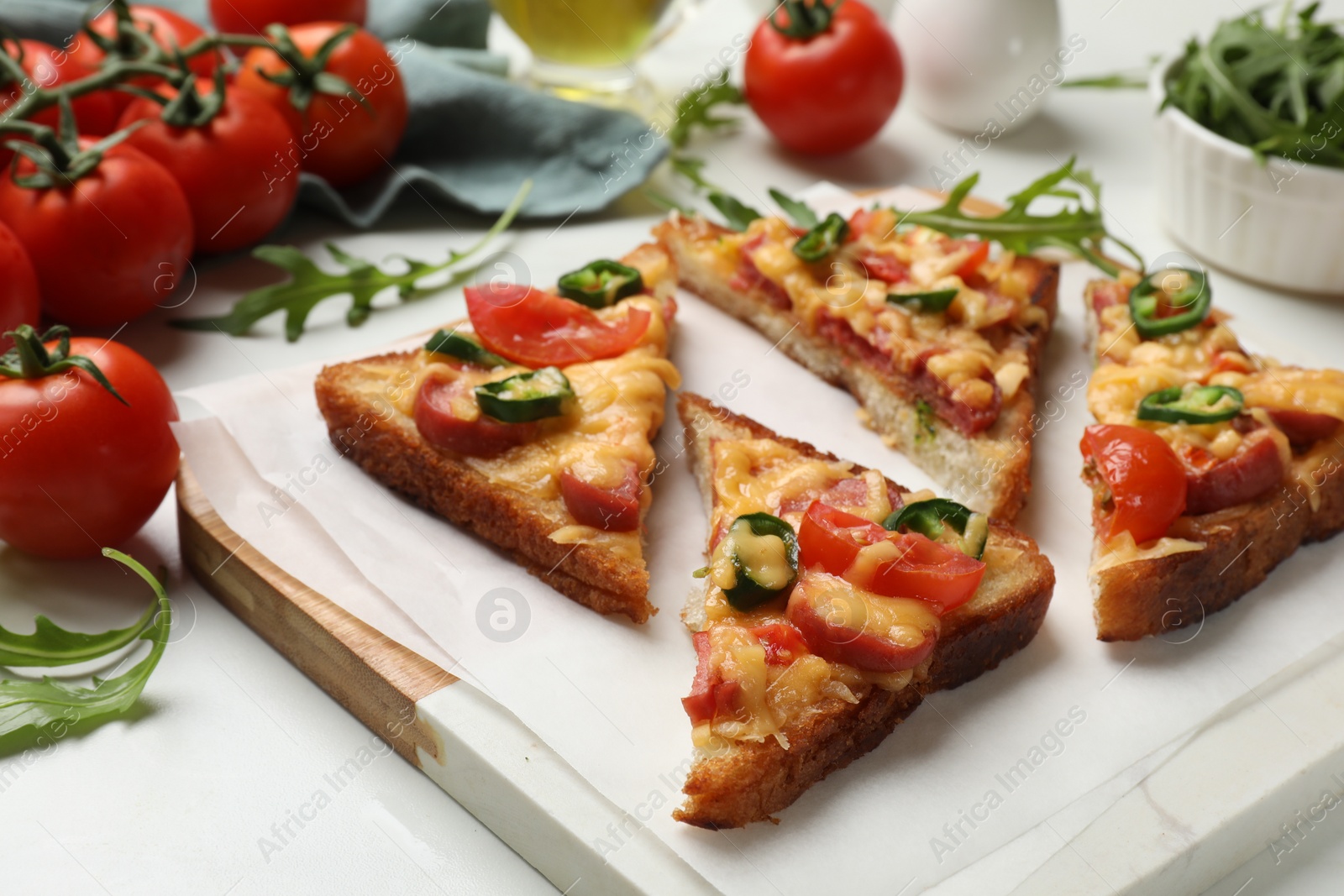 Photo of Tasty pizza toasts and ingredients on white marble table, closeup