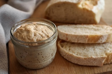 Photo of Sourdough starter in glass jar and bread on table, closeup