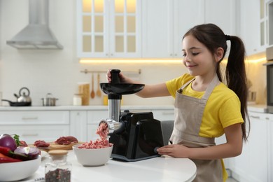 Photo of Little girl using modern meat grinder in kitchen