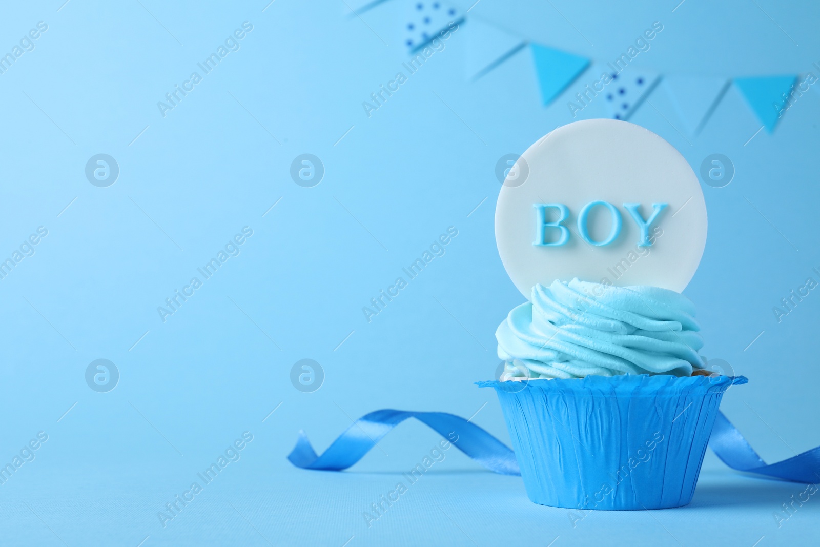 Photo of Beautifully decorated baby shower cupcake with cream and Boy topper on light blue background. Space for text