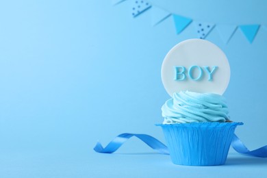 Beautifully decorated baby shower cupcake with cream and Boy topper on light blue background. Space for text